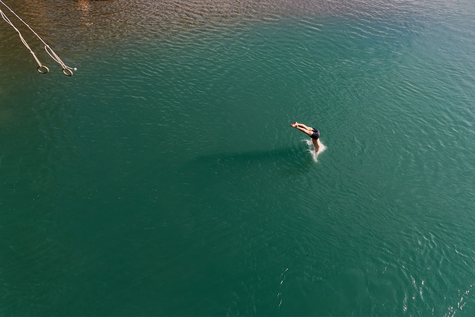 The image shows the photograph of a young man taking a header into a lake with green water. 