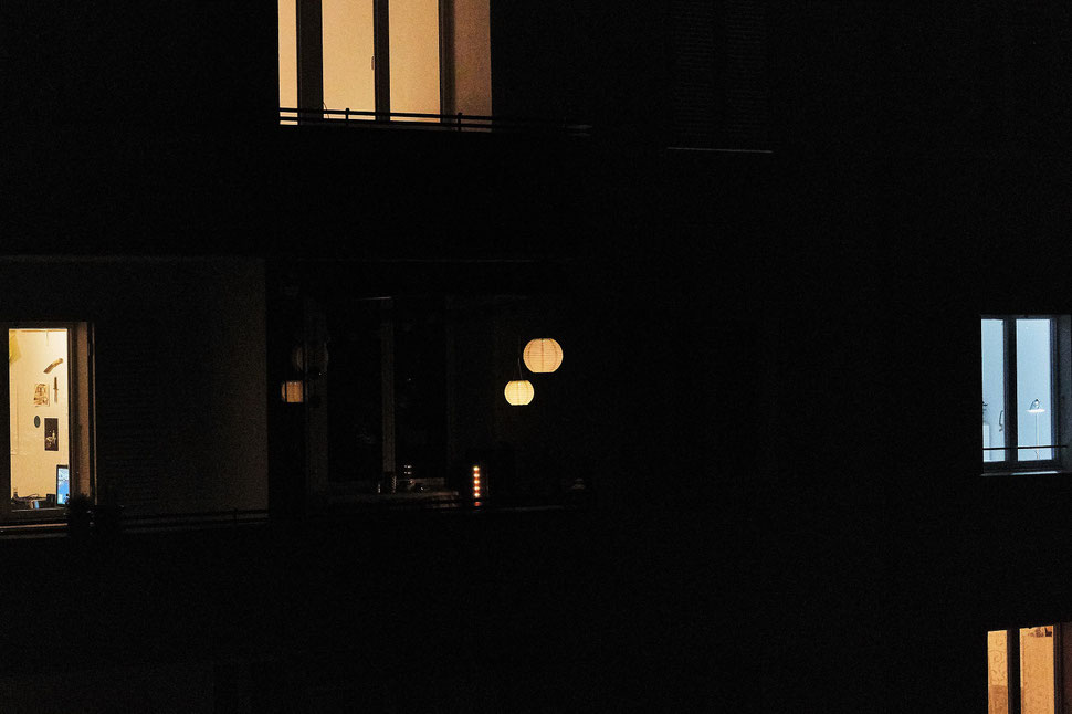 The image shows the night photograph of a the facade of an apartment building. Some windows are lighted, most are not. 