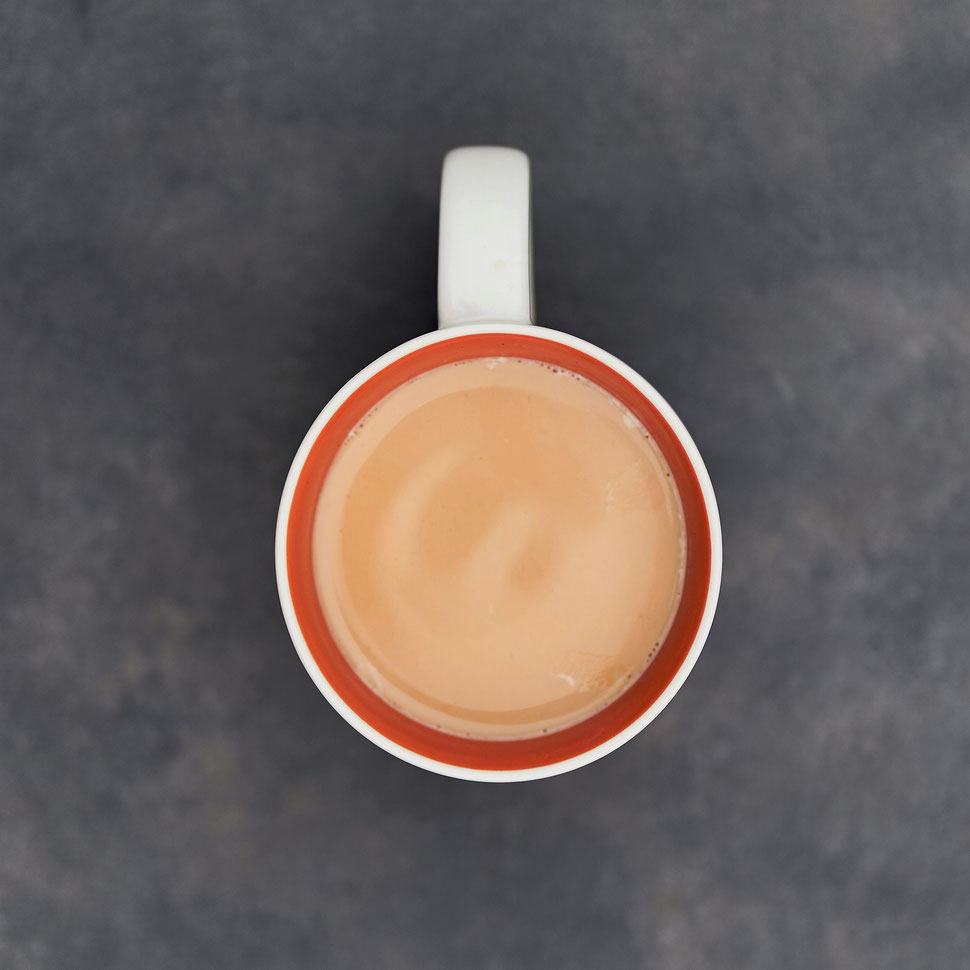 The image shows a a bird's eye view of a cup of coffee standing on the dark grey surface of a table.