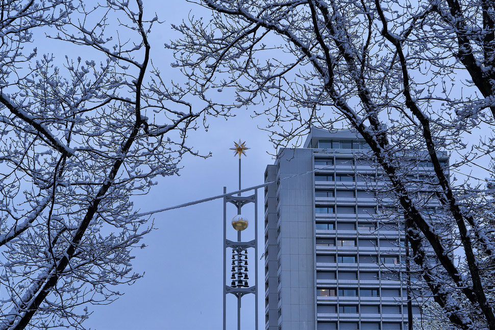 The image shows the photograph of bell tower with a star on top next to a high rise. There are snow covered branches of trees in the foreground. The locaion ist Bethlehem, which is in the west of Bern.