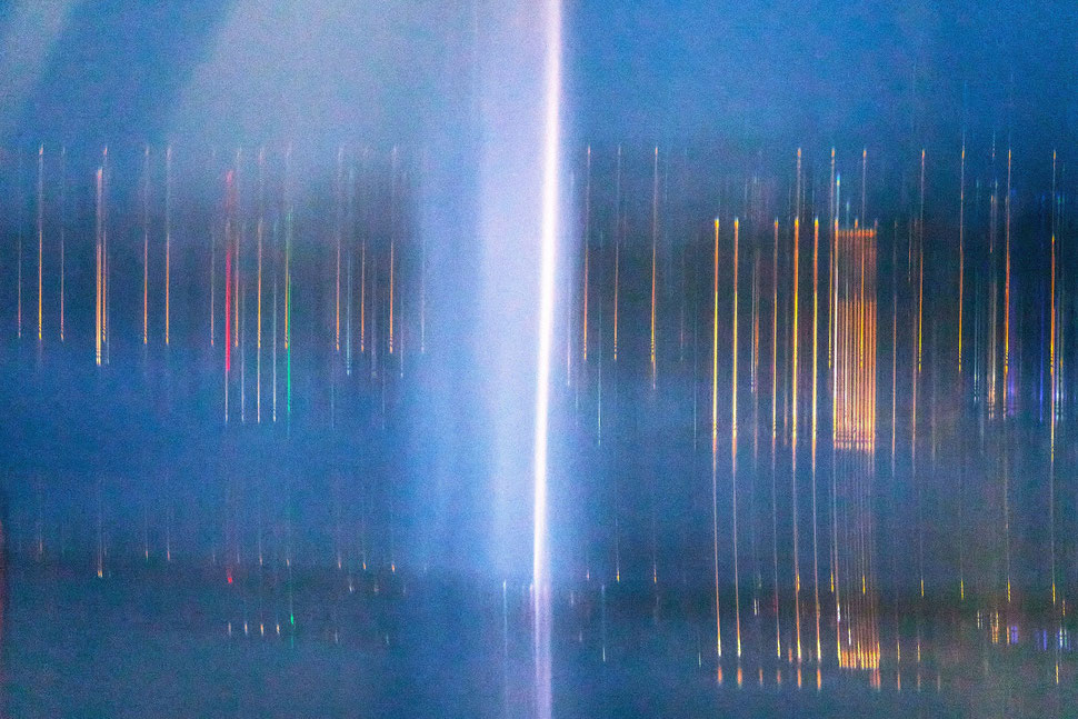 The image shows the night photograph of a blurred, colorful version of Geneva's famous water fountain called "Jet d'eau".