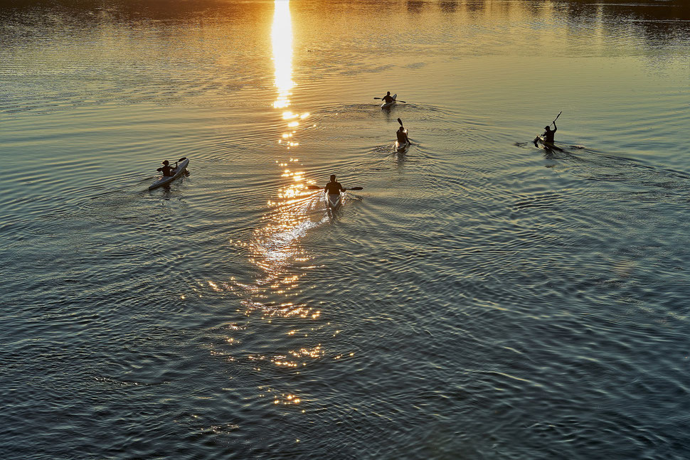 The image shows the photograph of five people kayaking in Wohlensee, a reservoir near Bern, during sunset.