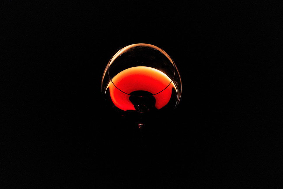 The image shows the photograph of a glass of wine, which is light by a candle against a black background.