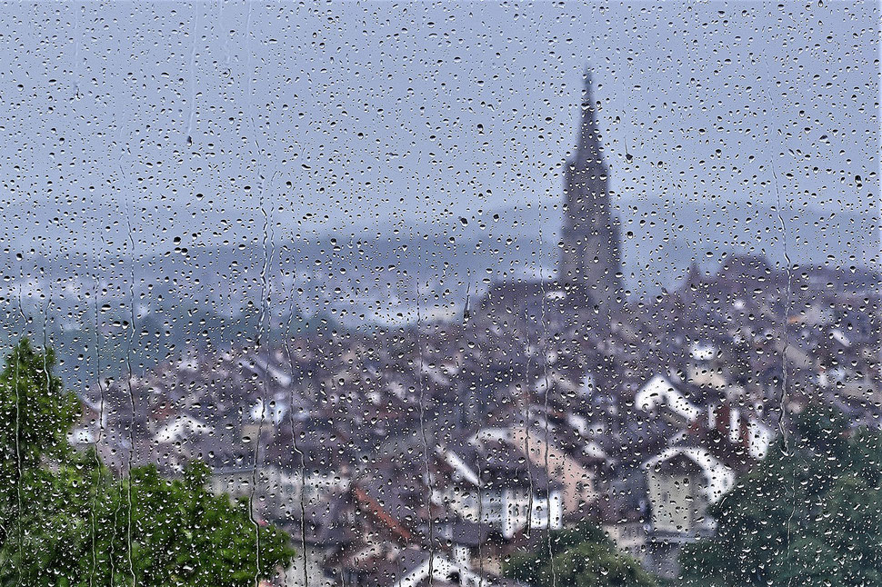 The image shows the blurred photograph of the old town of Bern through a window stained with raindrops.