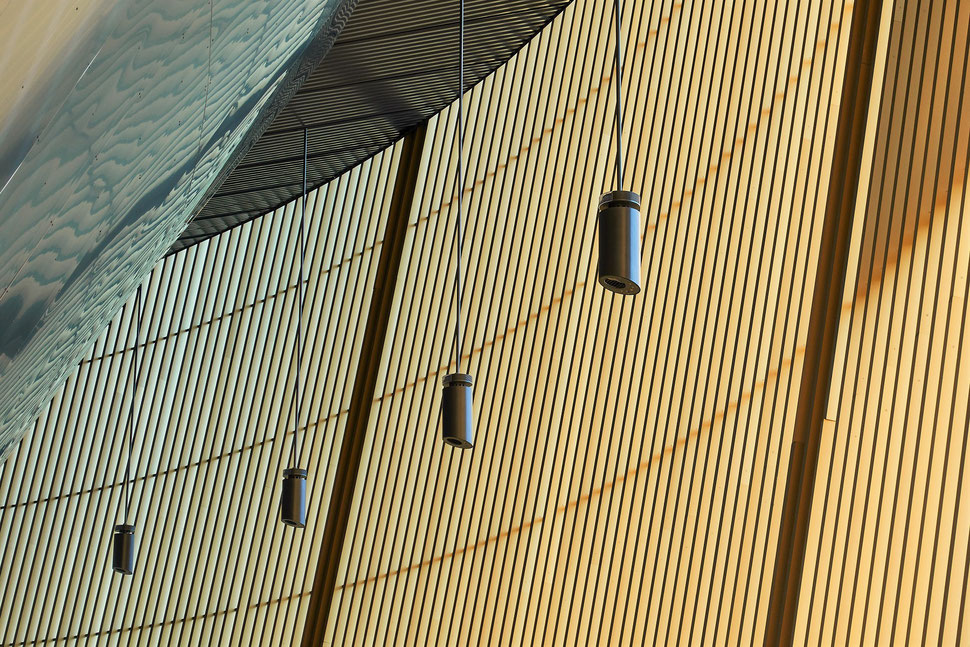 The image shows the photograph of a snippet of architectural wood structures and four hanging lamps in Lucerne's football stadium.