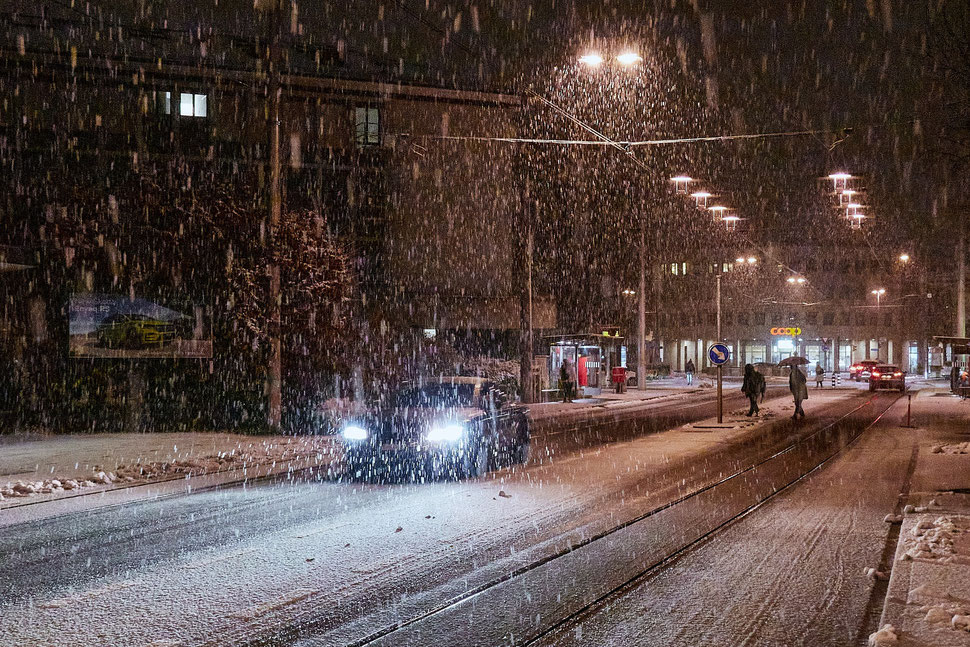 The image shows a night photograph of a car plowing throug a snow storm.