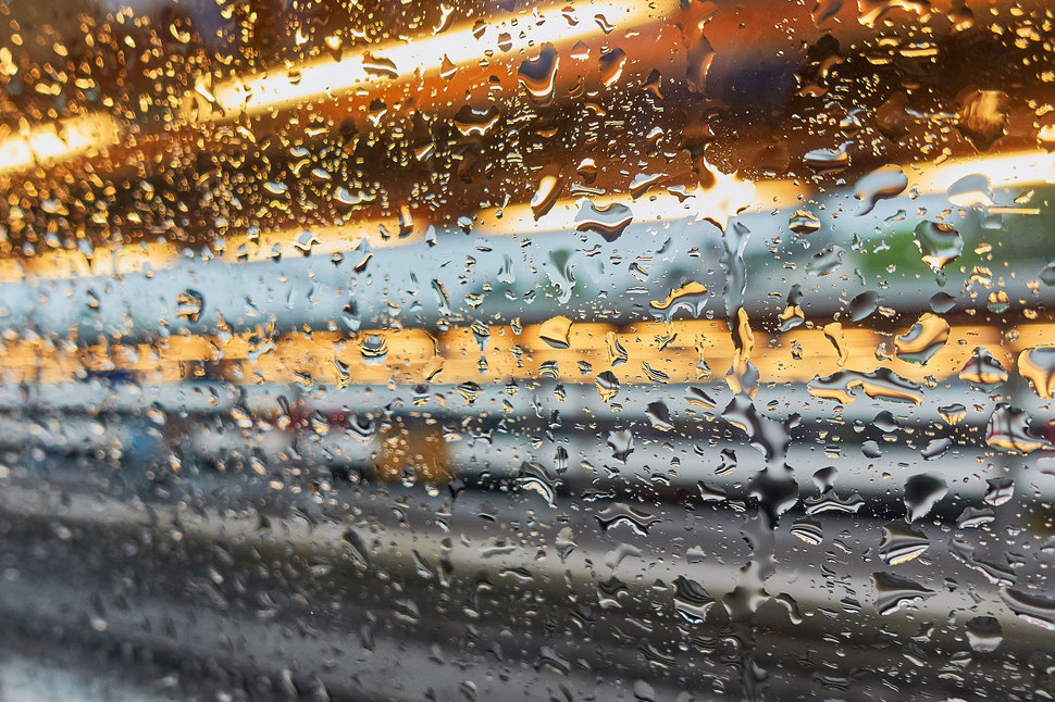 The image shows the abstract photograph of a train window with rain drops and streaks of light.