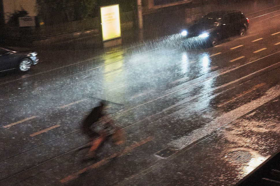 The image shows the photograph of a cyclist riding through a rain storm in the night.