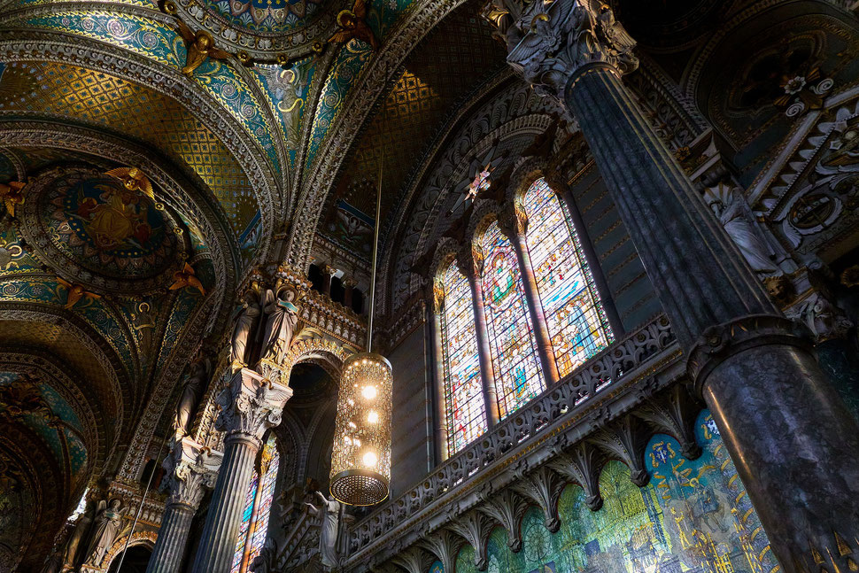 The image shows a photograph of the inside of the Basilica in Lyon whlie the evening light is pouring through the windows.