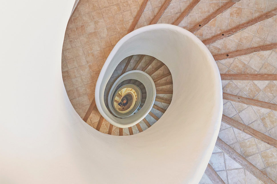 The image shows the photograph of a spiral staircase and a woman from above.