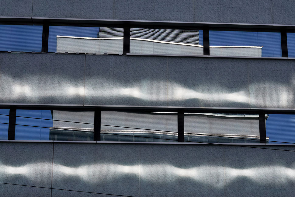 The image shows the photograph of a building facade with two rows of windows, which display multiple reflections of sunlight and another buidling.