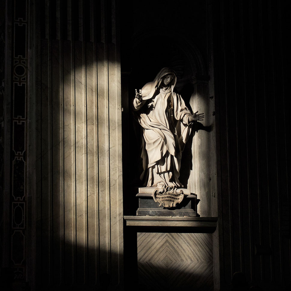The image shows the photography of a church statue, which is partly illuminated by sunlight. The sculpture is inside St. Peter's Basilica in Rome.