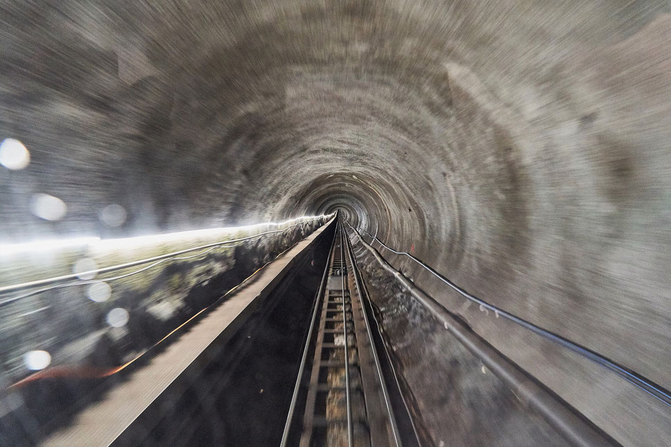 The image shows a photograph of a tunnel and tracks; the photo was taken through the rear window of a fast moving train.