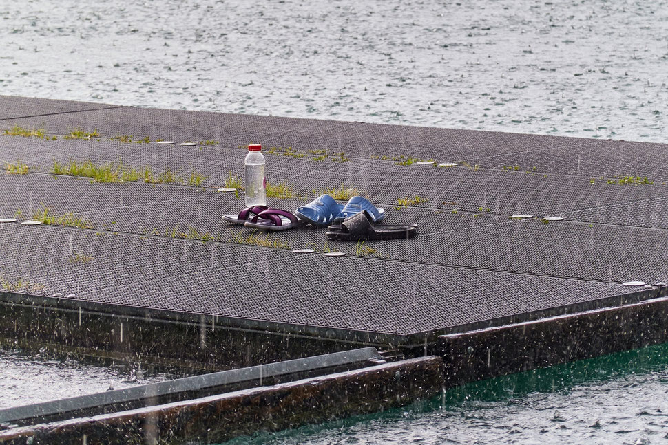 The image shows the photograph of three pairs of slipers on a ?? during a rainstorm. The location is Lake Wohlen in Eymatt (near Bern).
