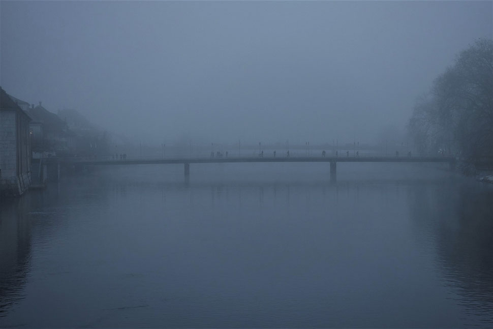 The image shows the photograph of People crossing a brindge in Solothurn on a foggy Winter day.