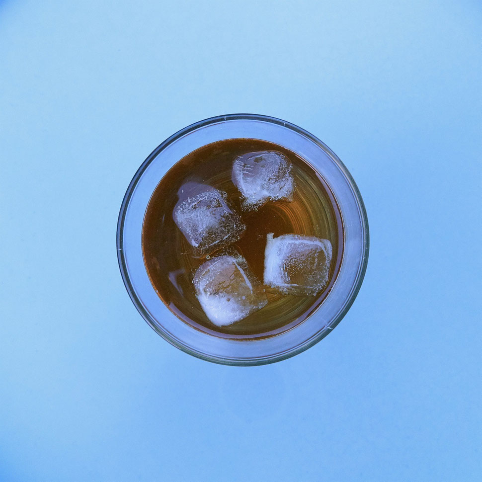 The image shows the aerial photograph of an enticing Summer drink with ice cubes on a blue surface.