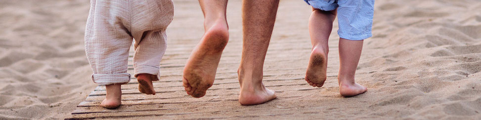 Vater mit zwei kleinen Kindern barfuß am Strand