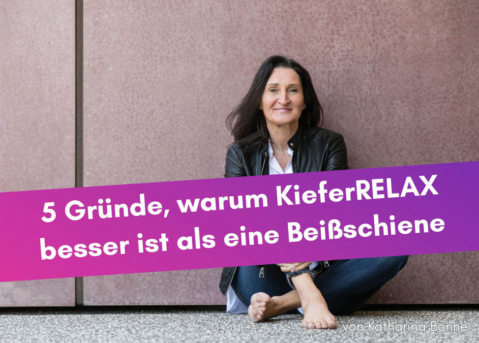 Frau mit Jeans, Bluse und schwarzer Lederjacke sitzt barfuß auf dem Boden und lächelt