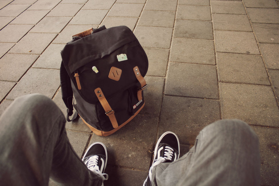 Junger Mann sitzt auf Fußweg mit Rucksack