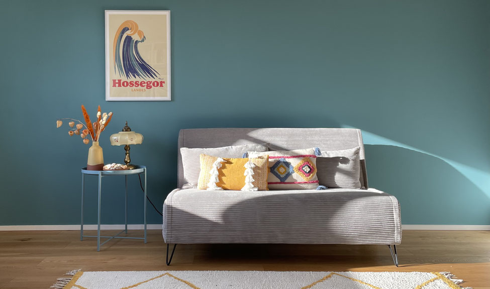 Wohnzimmer mit grauem Sofa, türkis farbener Wand und warmem Licht – stilvolle Raumgestaltung in Hamburg