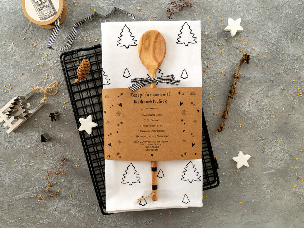 Weisses Küchentuch mit schwarzen Tannenbäumchen gestemptelt. Papier Banderole mit aufgedrucktem Rezept für Weihnachtsglück