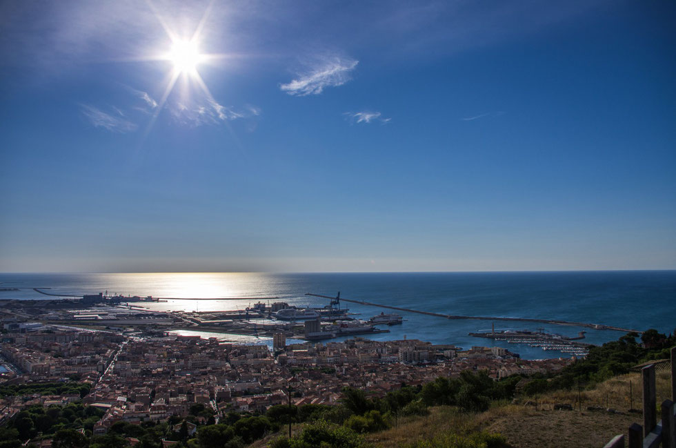Vue plein sud, de la ville de Sète et de son port depuis le sommet du Mont Saint Clair, la mer est d'huile son bleue profond se prolonge dans le dégradé du ciel avec deux petits nuages, et le soleil de face irradie à sa surface #provence#ayniart#art