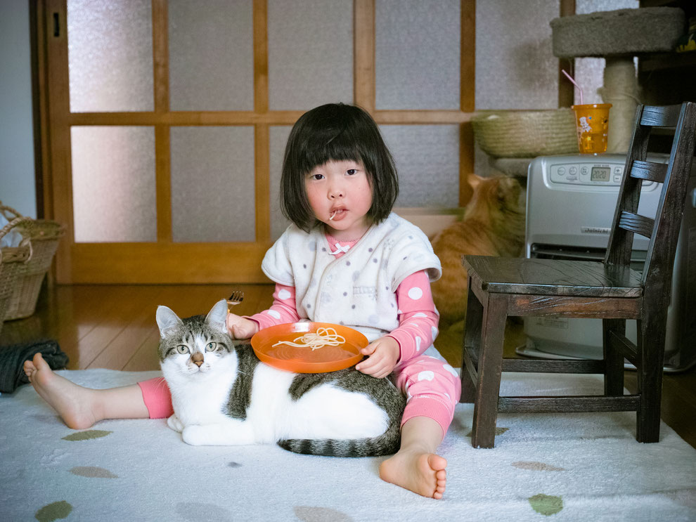 猫の上にお皿を乗せてごはんを食べる女の子