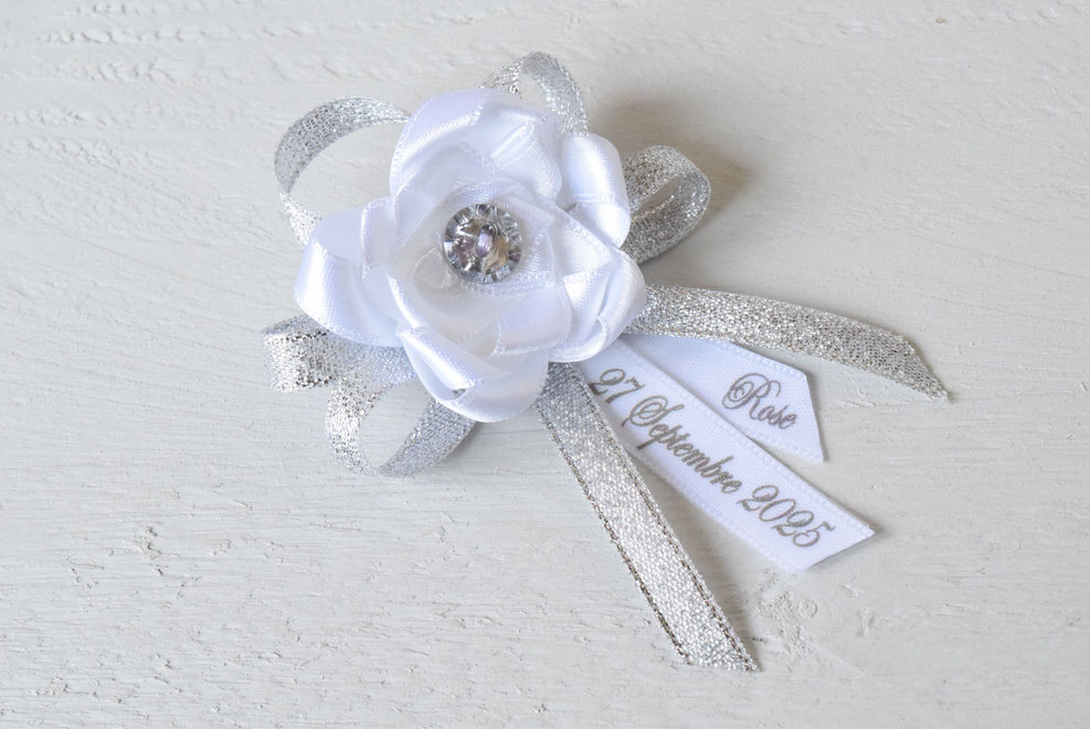 Création unique pour le grand jour, une jolie broche fleur blanche et argenté. Ruban imprimé date + prénom au choix. Création personnalisée avec le prénom et date du baptême.