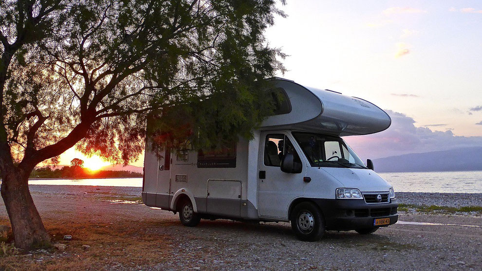 Ein Wohnmobil am Strand im Sonnenuntergang. Caravaning-Urlaub boomt in der Corona-Zeit. Gut geschützt mit einer Camping-Reiseversicherung und CDW-Versicherung der ERGO.