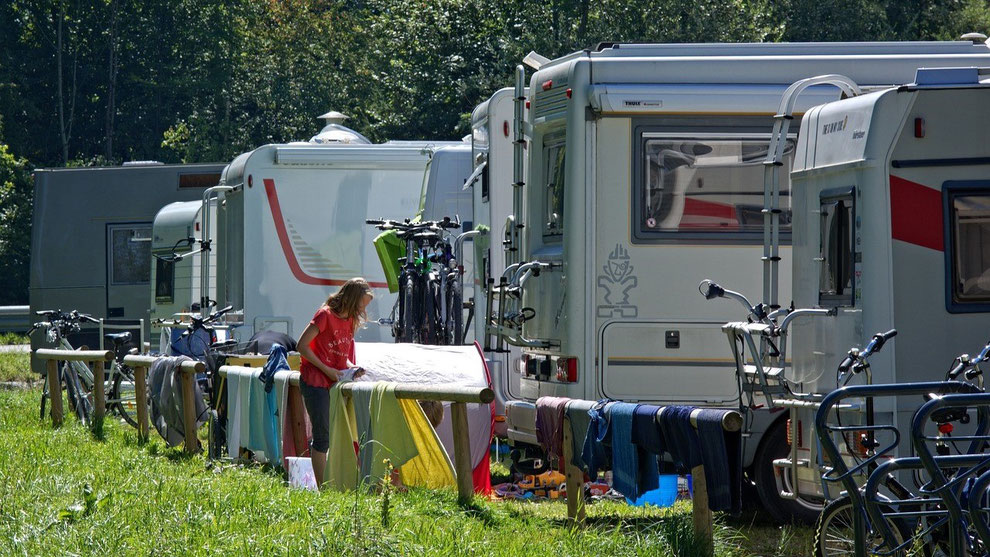 Mehrere Wohnmobile auf einem Campingplatz. Eine Frau hängt Wäsche auf. Camping-Urlaub boomt in der Corona-Zeit. Gut geschützt mit einer Camping-Reiseversicherung und CDW-Versicherung der ERGO.