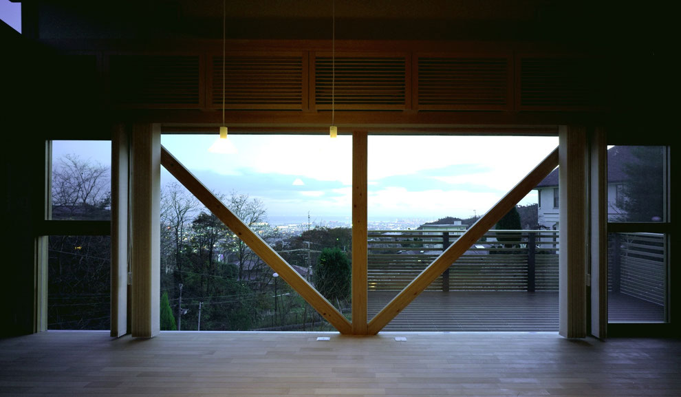 平賀敬一郎建築研究所が設計した、斜面地に建つモダン住宅のリビングから望む眺望。V字の木造構造材を額縁に見立て、街のパノラマビューを絵画のように切り取る設計。