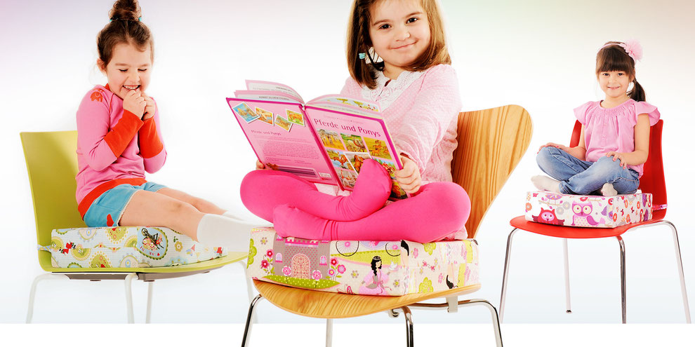 Drei Mädchen im Alter von ca. 3-5 Jahren sitzen auf verschiedenen Stuhl Sitzerhöhungen