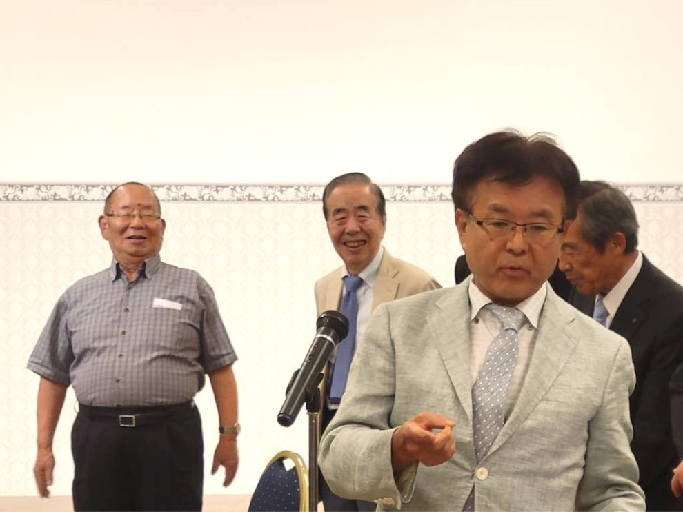 【マイク前】熊谷高校同窓会　本庄支部幹事　飯塚 明男氏（高24回）／【後列左】立石秀壽氏（本庄支部顧問・高12回）、【後列左から2番目】渋谷修身氏（本庄支部顧問・高12回）