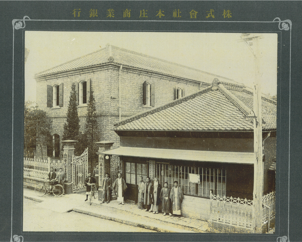 （右手前）「本庄商業銀行」　　（左奥）「旧本庄商業銀行煉瓦倉庫」　　　※本庄商業銀行前に並ぶ右から三番目の髭の人物が戸谷家11代目の戸谷八郎左衛門です。