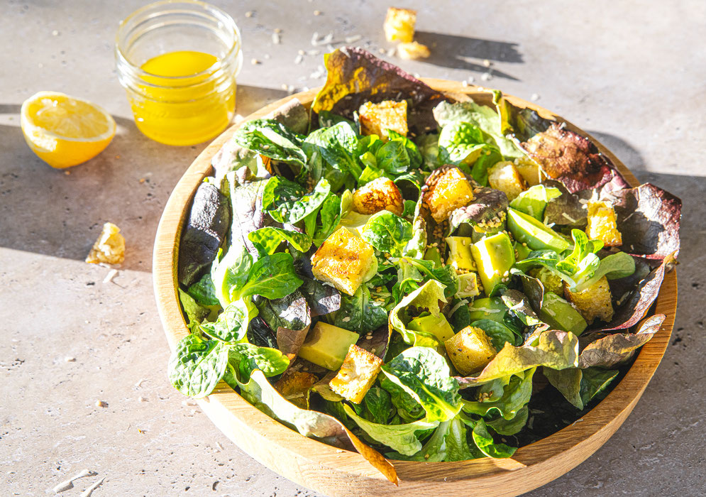 Knackiger Blattsalat mit gerösteten Ciabatta-Würfeln, Avocado und frisch geriebenem Parmesan, serviert in einer Holzschale.