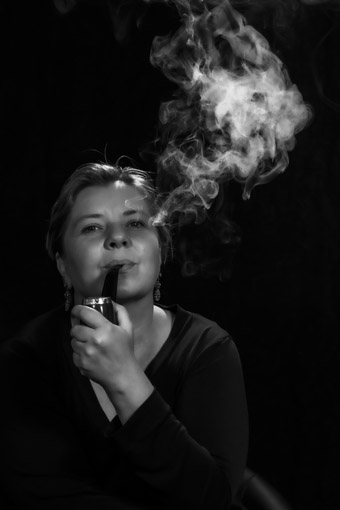 Die Fotografie zeigt Antje Lindner eine Pfeife rauchend vor schwarzem Hintergrund