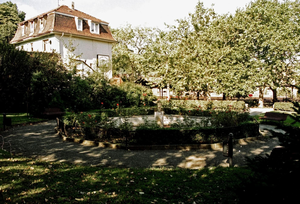 Kleiner Park gegenüber vom Bahnhof. Im Hintergrund das Kino.