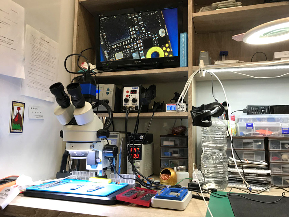 修理作業スペースに、顕微鏡や基板確認用モニター、修理工具、部品ケースが並んでいる写真。スマホ修理や基板修理、細かな部品交換に対応する設備の様子。