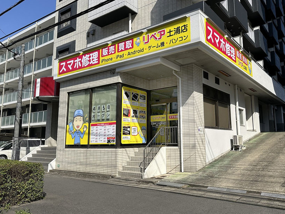 リペア土浦店の建物外観と、スマホ修理、販売、買取を案内する黄色と赤の看板が見える写真。iPhone、iPad、Android、ゲーム機、パソコン修理に対応する店舗。