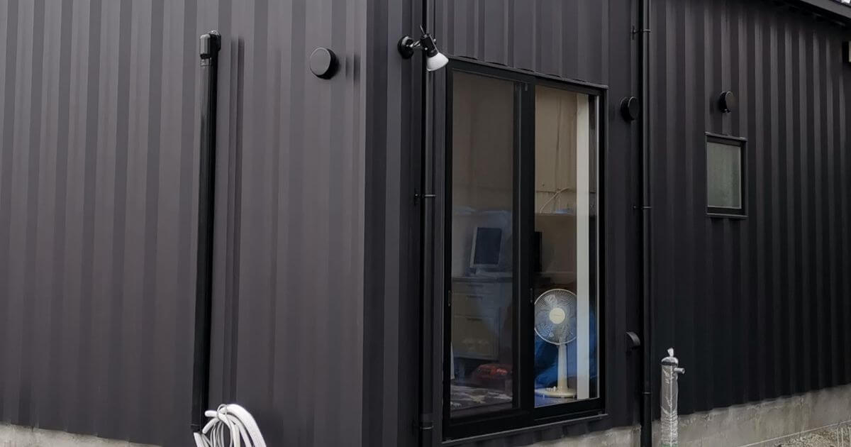 北側の掃き出し窓と小窓まわりの施工ディテール。ビス隠し仕様により、リブの縦ラインが途切れず通っている。縦樋や外部照明配管も壁色に合わせて統一されている。