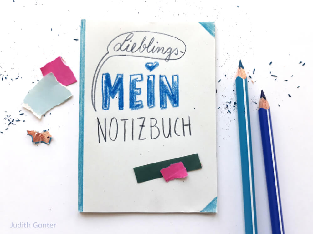 Titel: „Mein Lieblingsnotizbuch“ – Sketchnotes-Beispiele im Notizbuch, daneben zwei blaue, frisch angespritzte Buntstifte.