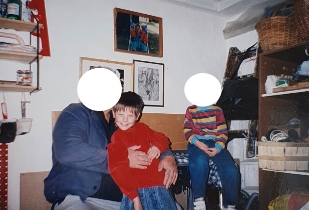 Auf dem Bild von 1997 bin ich 7 Jahre alt. Außerdem sind mein Opa und mein jüngerer Bruder in der Werkstatt meines Opas zu sehen. Mein Opa hat seine Hände um meinen Bauch gelegt und ich lache in die Kamera. Mein Bruder sitzt auf einem kleinen Tisch.
