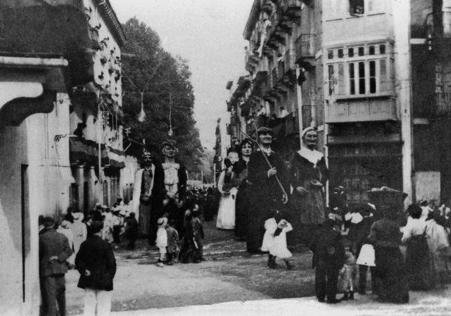 Comparsa de gigantes y cabezudos, precediendo a la procesión celebrada con motivo de la festividad de San Miguel, patrón del ámbito de La estación (la escena es anterior a 1911). Fotografía tomada en la Calle Zibiaurre, y cedida por José María Castillo.