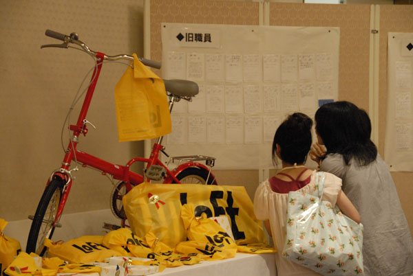 赤い折り畳み自転車は、ビンゴの景品です。 その後ろのつい立には、旧職員や各回生からのメッセージ（返信はがき）です。