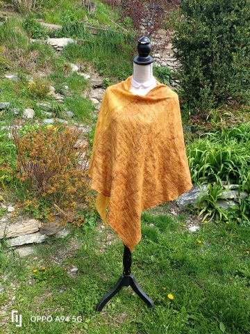 Mannequin posé dans un jardin, portant un poncho fait de laine mérinos, chameau, alpaga et soie, feutrés sur de la gaze de soie de marguilan. tons jaune d'or