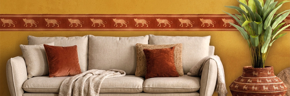 Wohnzimmer mit beigem Sofa und einer weinroten Ethno-Wandbordüre, die goldene Leoparden auf ockerfarbener Wand zeigt.