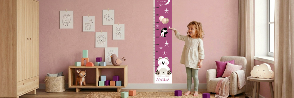 Mädchen im altrosa Kinderzimmer neben einer violetten Kindermesslatte mit Eisbär und Pinguin 