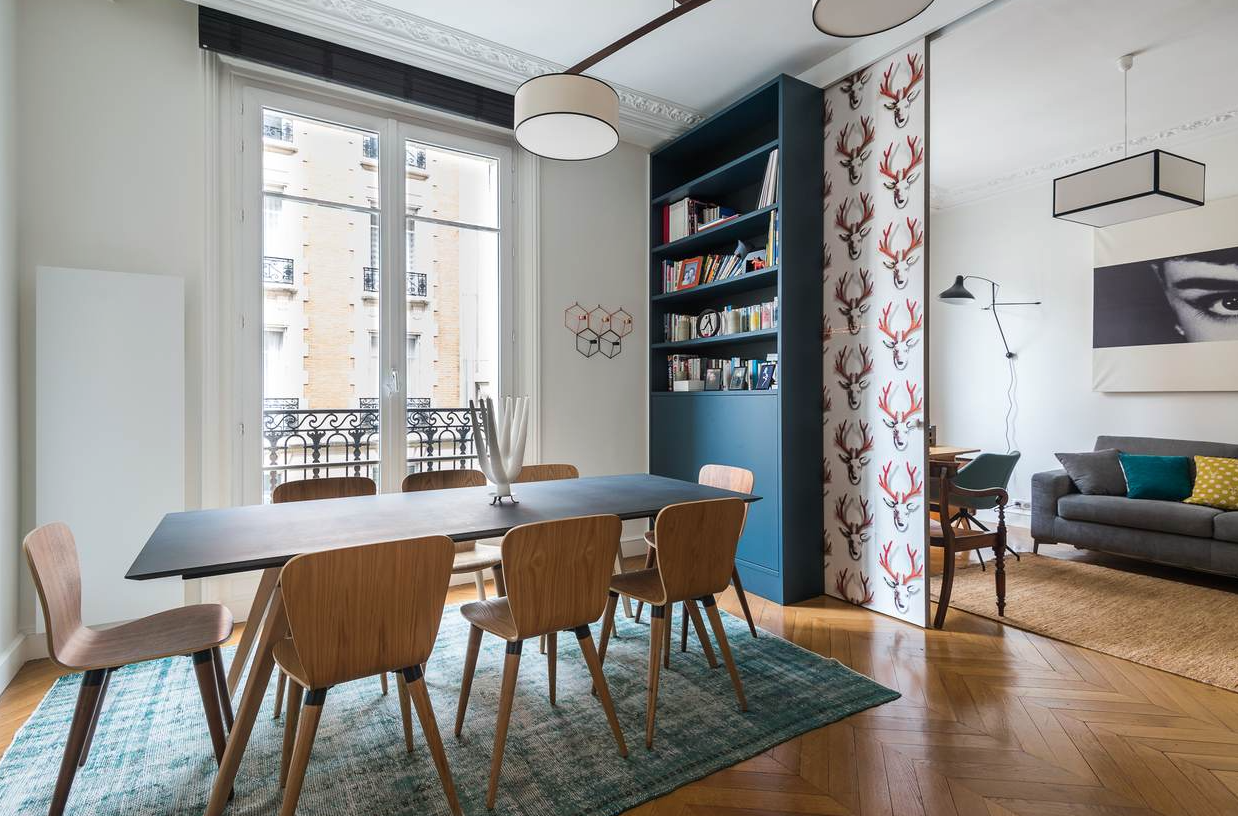 La bibliothèque sur mesure, peinte en cabine, avec portes coulissantes et ses stickers en tête de cerf. La cliente a choisi un mobilier de style scandinave et des stores à lattes bois noires.