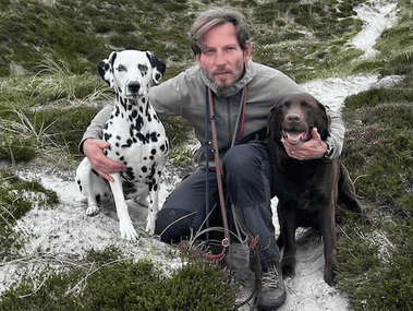 Foto von Oliver Grimm der zwei sitzende Hunde umarmt, links ein Dalmatiner und rechts ein Labrador.