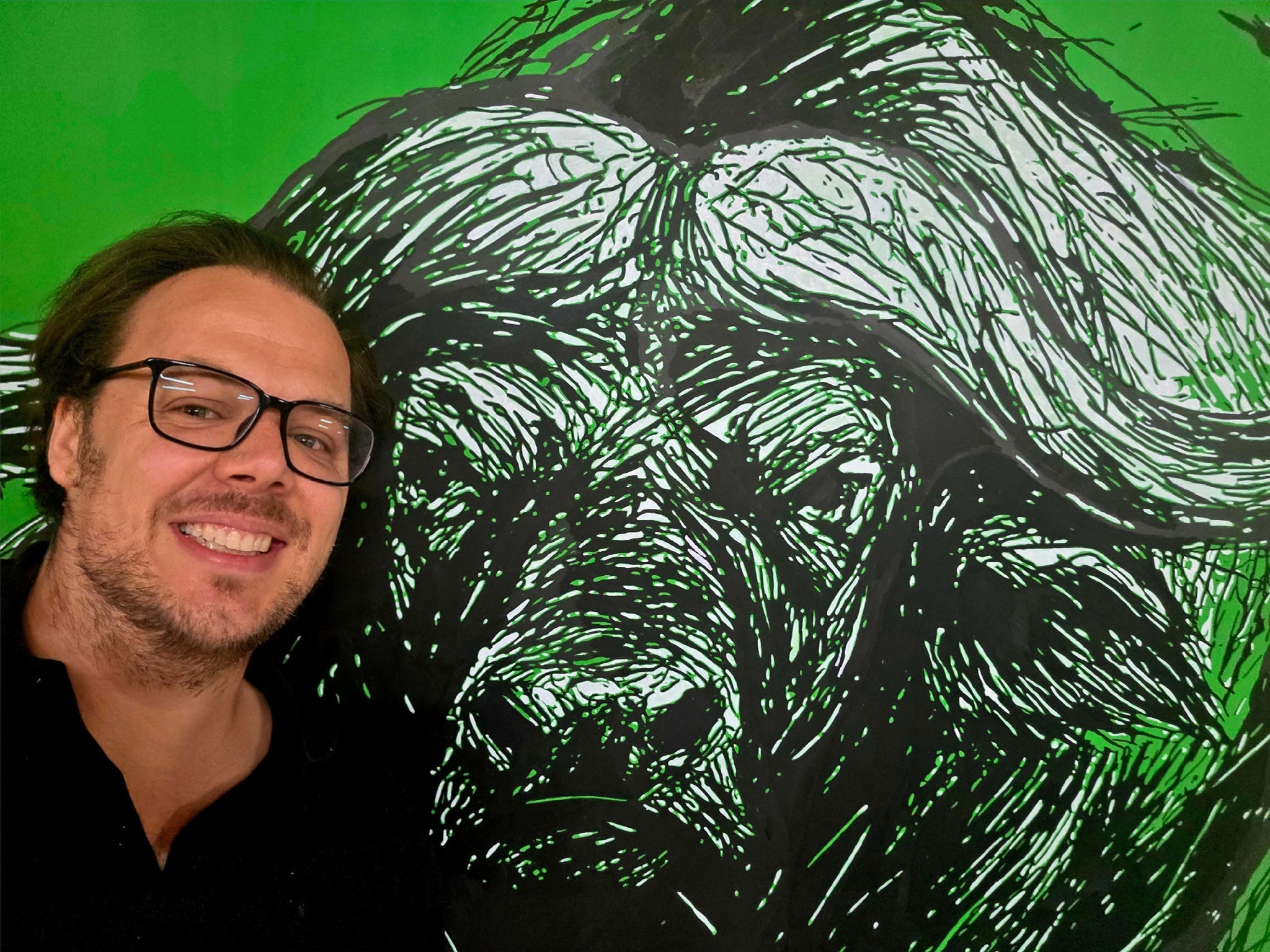 Nahaufnahme von "THE WALL HAS EYES" mit Künstler, Kunstwerk/Gemälde von Martin Lingens, schwarz-weißer Afrikanischer Büffel auf grünem Hintergrund